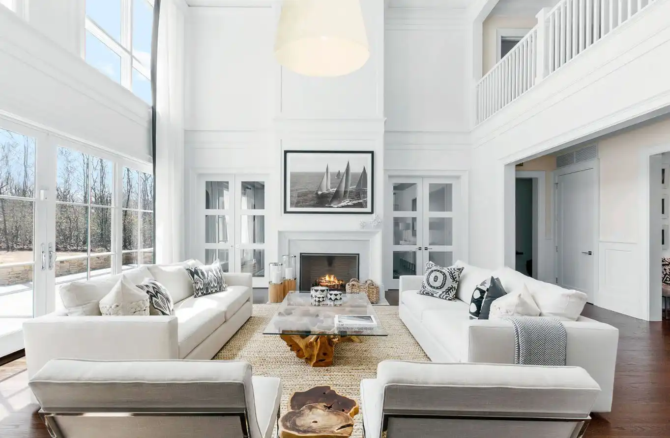 This double-height living room is furnished with two comfortable white sofas and matching armchairs, featuring a beach-inspired decor