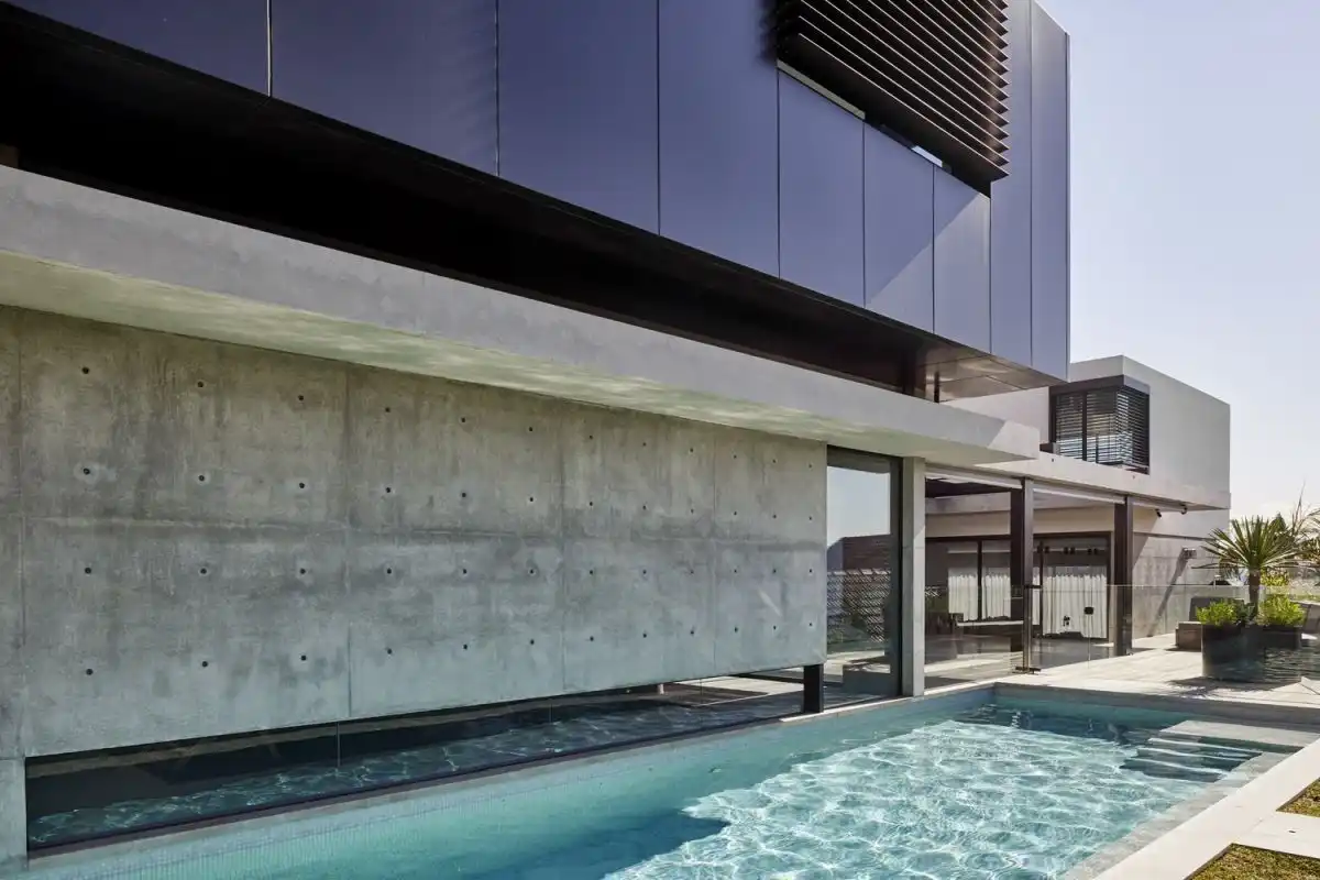The pool runs along the side of the house, bounded by a glass wall.