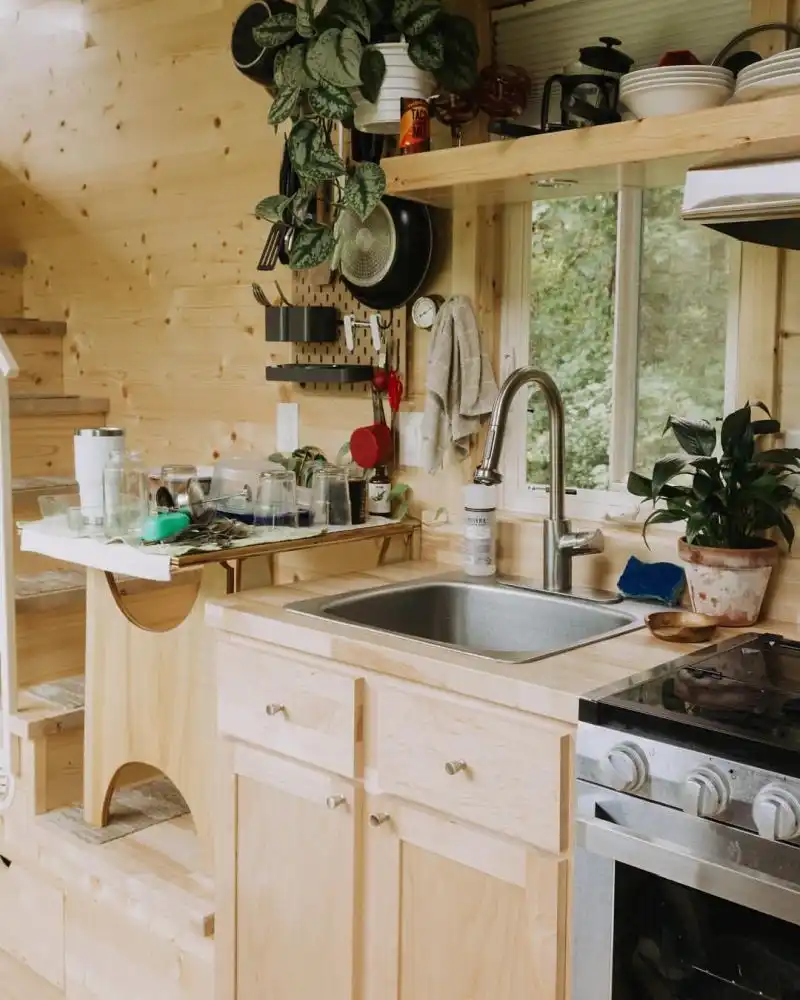 The kitchen is small but well-equipped, with storage shelves and a window in front of the sink