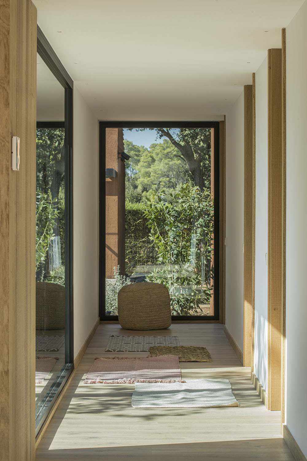 A hallway ends in a large window, leading the eye to the trees outside.