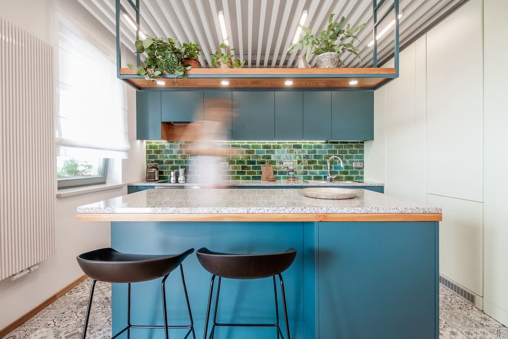 Blue kitchen cabinets with green tiles and suspended shelves above island