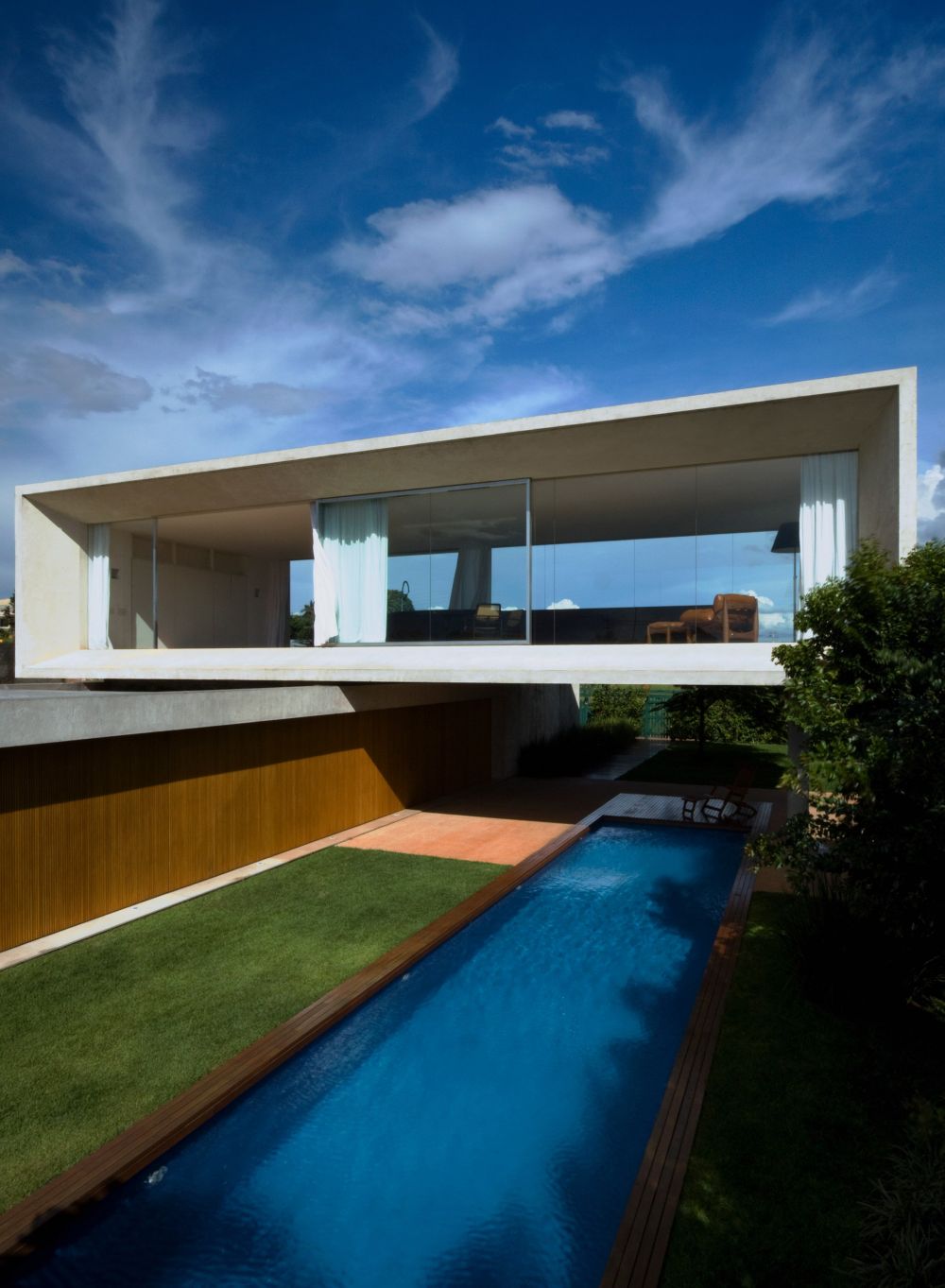 The top volume has glazed sides and hovers over a lap pool, being suspended on stilts
