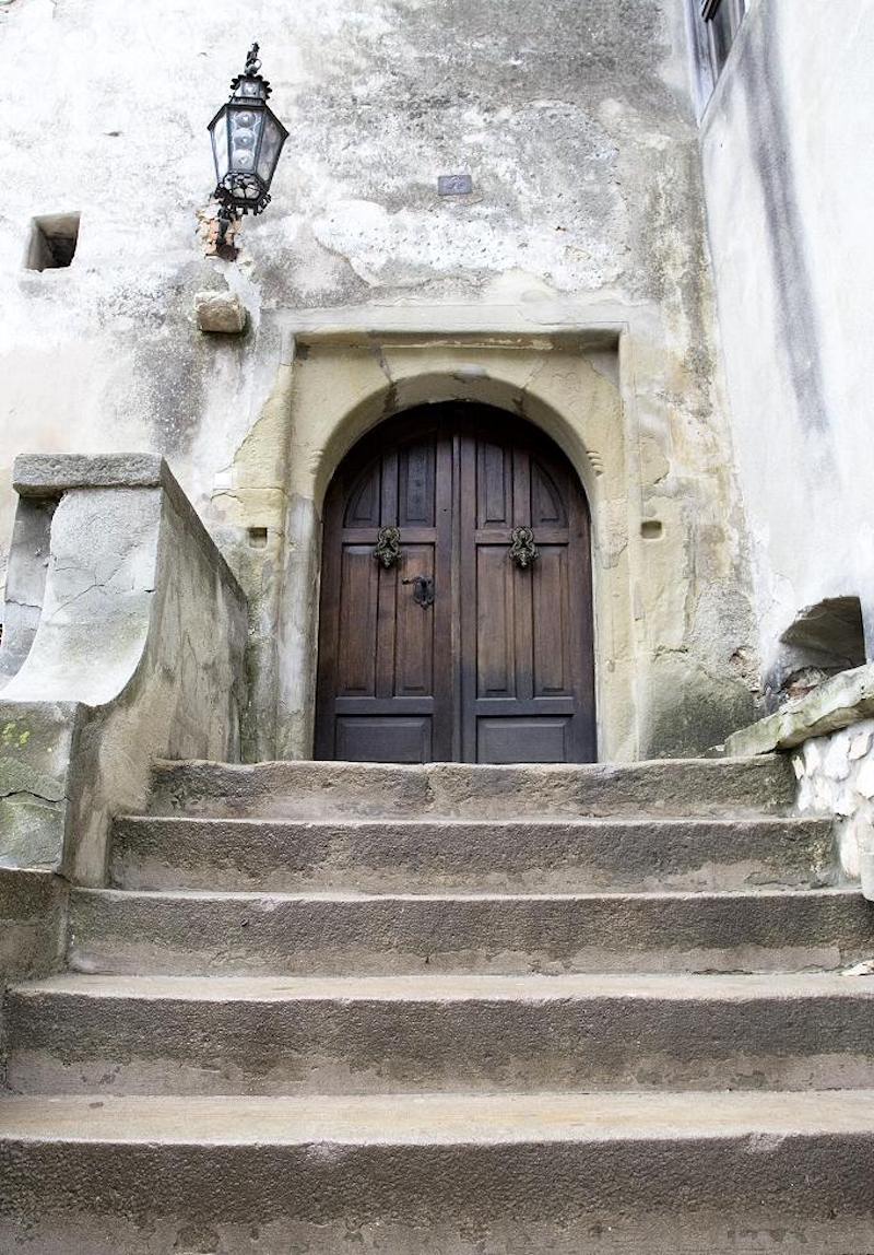 Visitors are welcomed inside the castle through a massive pair of wooden doors at the stop of a concrete staircase