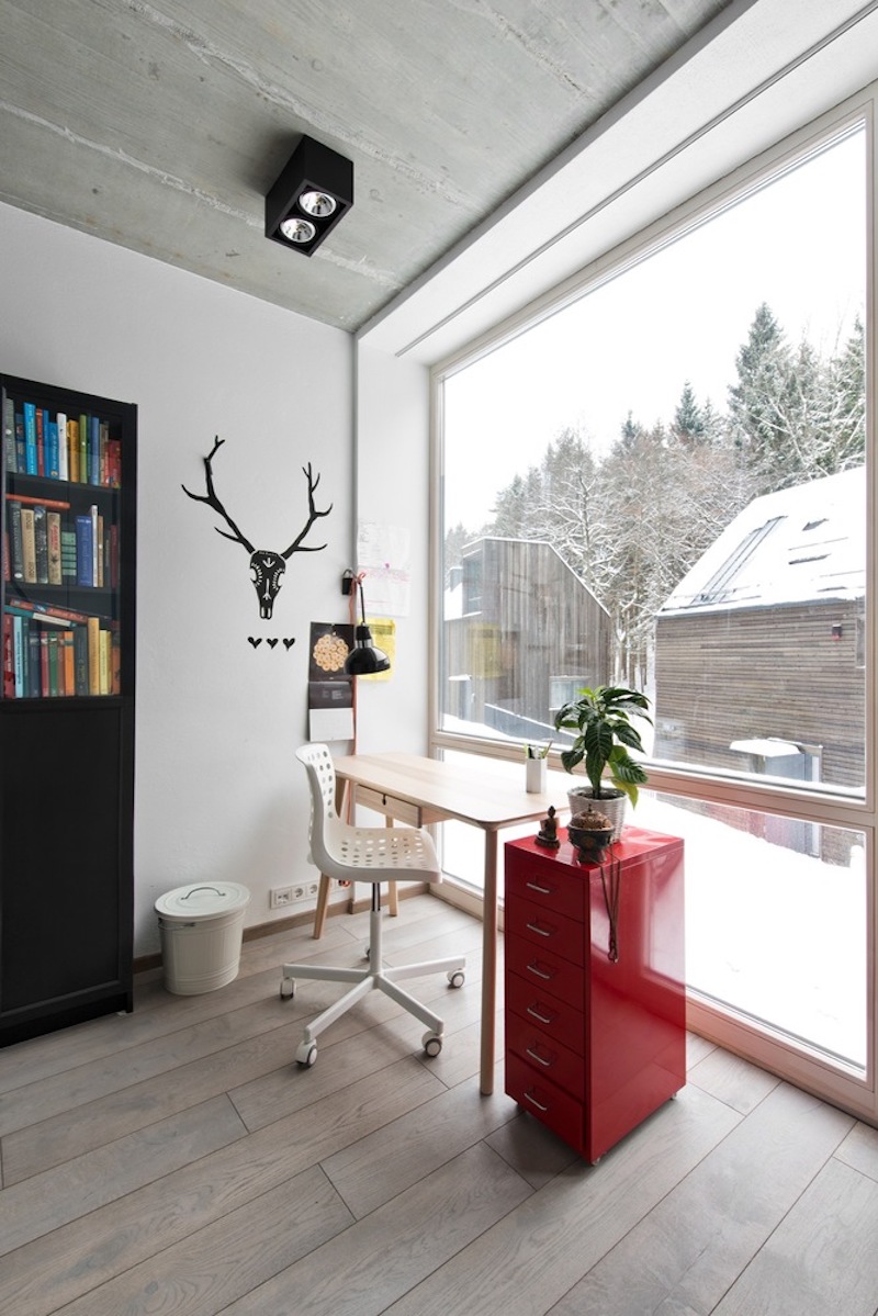 A small desk is positioned in front of a full-height window, featuring a funky red cabinet to its right