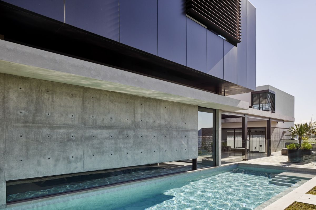 The pool runs along the side of the house, bounded by a glass wall.