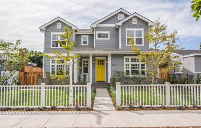 Traditional exterior grey house with bold yellow front door and white picket fence