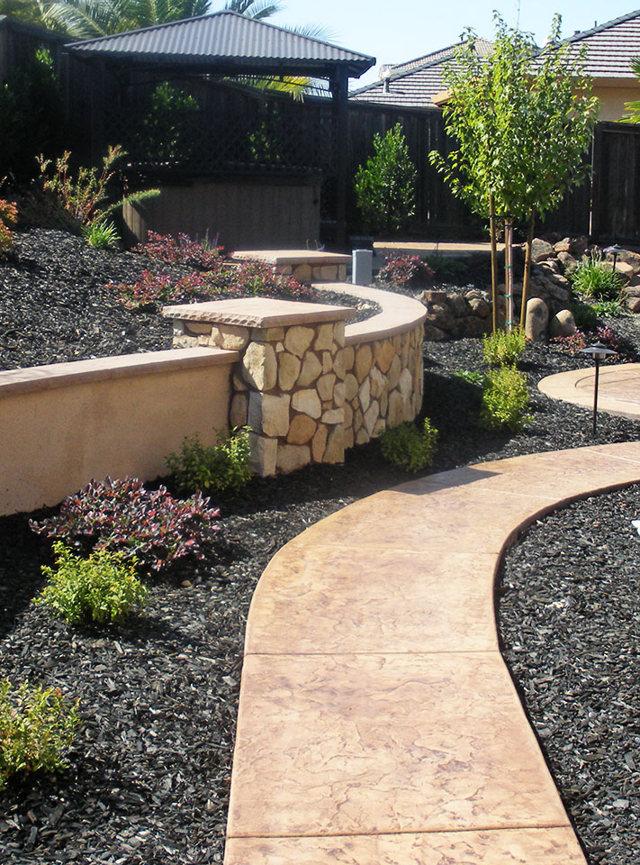 Backyard rock retaining wall planter stamped concrete path