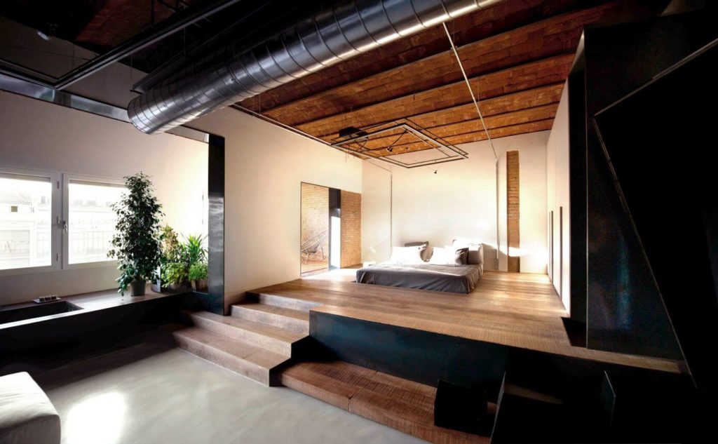 The bed is elevated on a platform, separating it from the bath area without dividing the space visually.