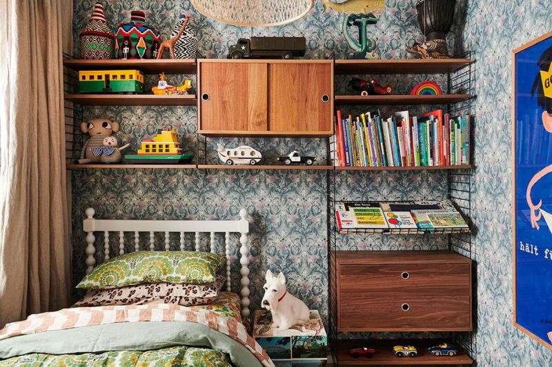 Childrens room with bookshelf and toys and a wall with flowered blue wallpaper