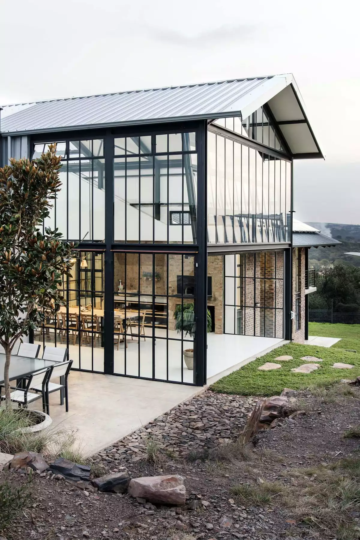 The double-height glass volume has a gabled roof and is filled with indoor plants which strengthens the connection between the house and the outdoors